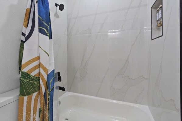 A bathroom with a white bathtub, a shower curtain with a tropical leaf pattern, and marble walls.