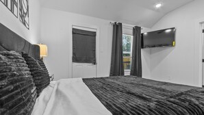 A bedroom with a bed, a TV mounted on the wall, a door, and a window with curtains. - Spacious ,Luxury 3-bedroom apartment in Houston with Games ,Smart Tv,Wifi (Houston)