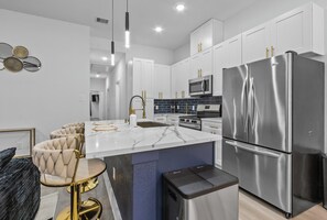 A modern kitchen with white cabinets, stainless steel appliances, and a marble island.