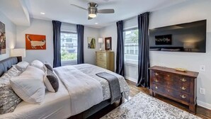 Une chambre à coucher moderne, dotée d’un grand lit, d’un ventilateur de plafond, d’une commode et d’un téléviseur à écran plat fixé au mur.