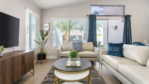 A living room with a sofa, a coffee table, a TV, and a window with blinds.