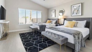 A modern bedroom with a bed, bedside tables, a desk, a chair, a ceiling fan, and a window with blinds.