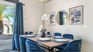 A dining area with a wooden table set for six, blue upholstered chairs, and framed artwork on the wall.