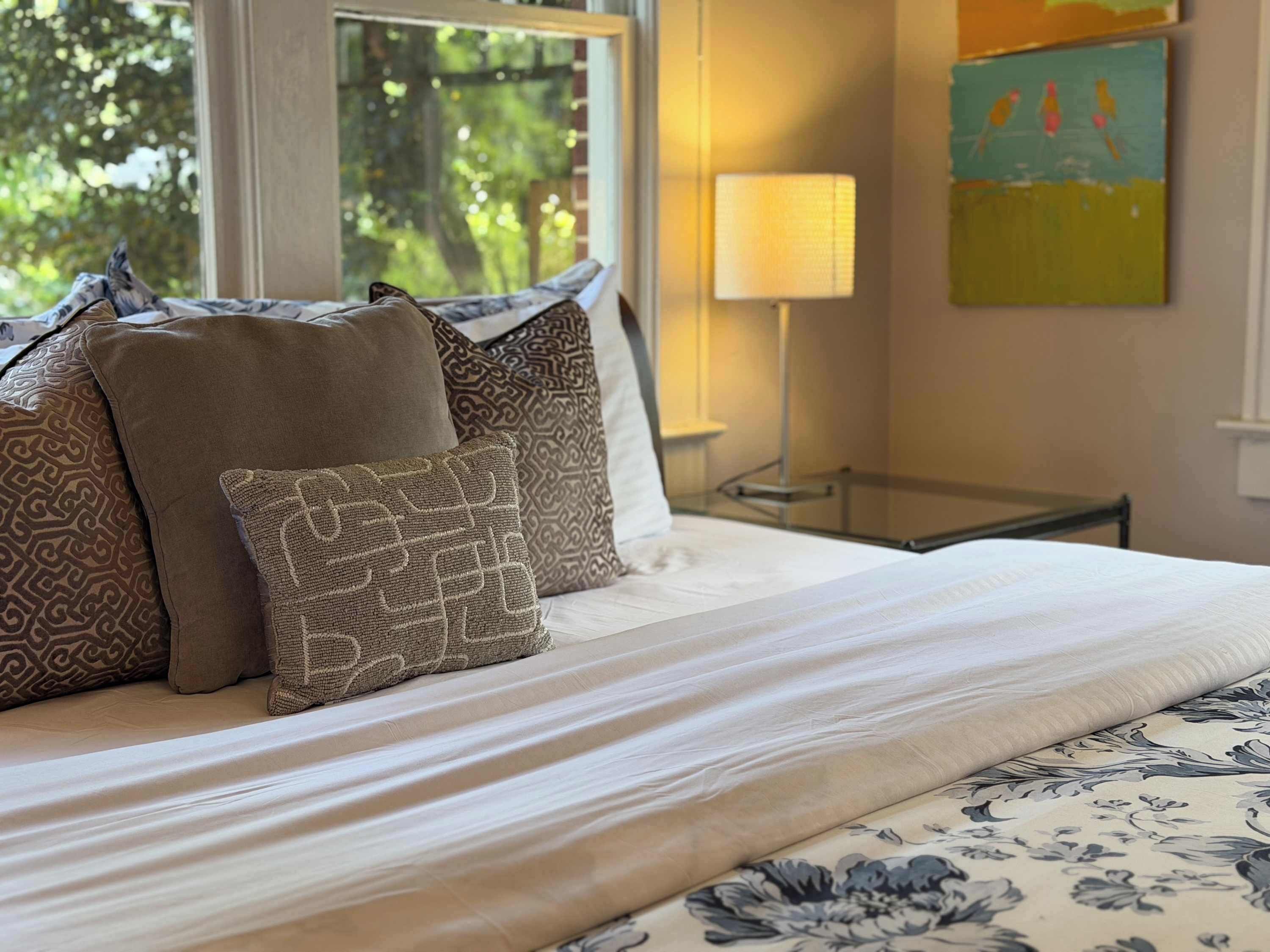 Een net opgemaakt bed met gestreepte kussens, een bedlampje en een bloemenprintdeken.