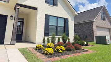 A two-story house with a brick facade, a front porch, and a well-maintained garden with various shrubs and flowers.