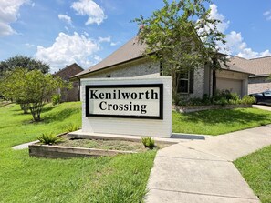 A sign for Kenilworth Crossing with a brick building in the background. - Tigers Geaux Crazy at The Wild LSU Jungle - KC7049 (Baton Rouge)
