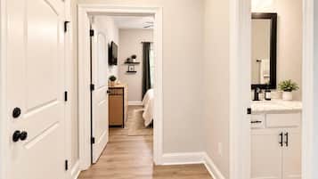 A hallway with white doors, a wooden floor, and a bathroom with a mirror, sink, and towel rack.
