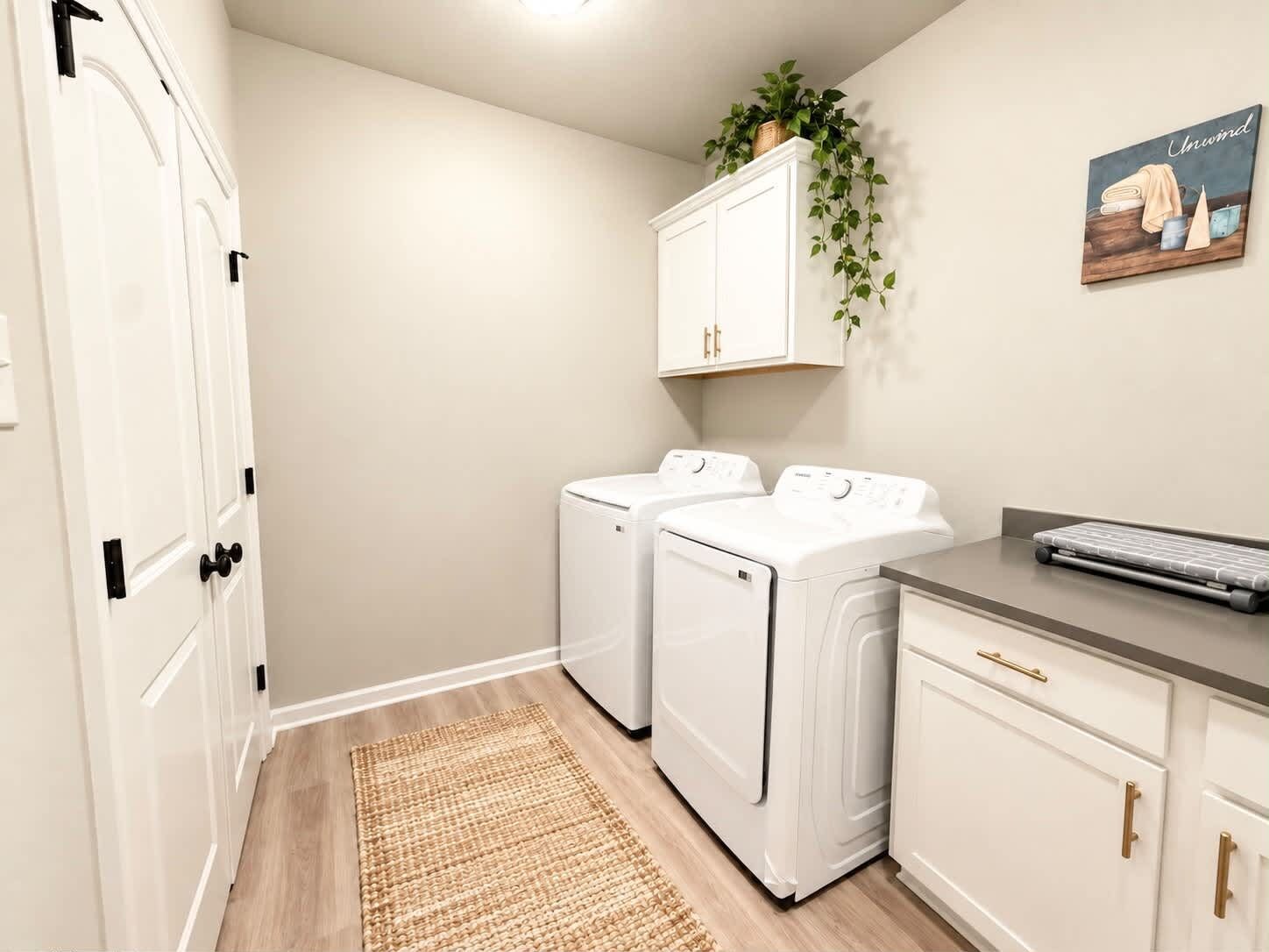 A laundry room with two front-loading washing machines, a drying rack, and a small desk with a keyboard.