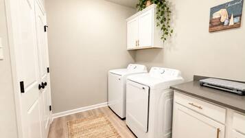 A laundry room with two front-loading washing machines, a drying rack, and a small desk with a keyboard.
