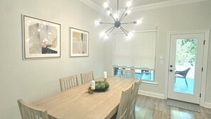 Una sala da pranzo con un tavolo in legno, sei sedie, un lampadario e due opere d'arte incorniciate al muro.