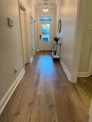 A hallway with wooden flooring, a door with a window, and a small table with a plant. - Tigers Geaux Crazy at The Wild LSU Jungle - KC7049 (Baton Rouge)