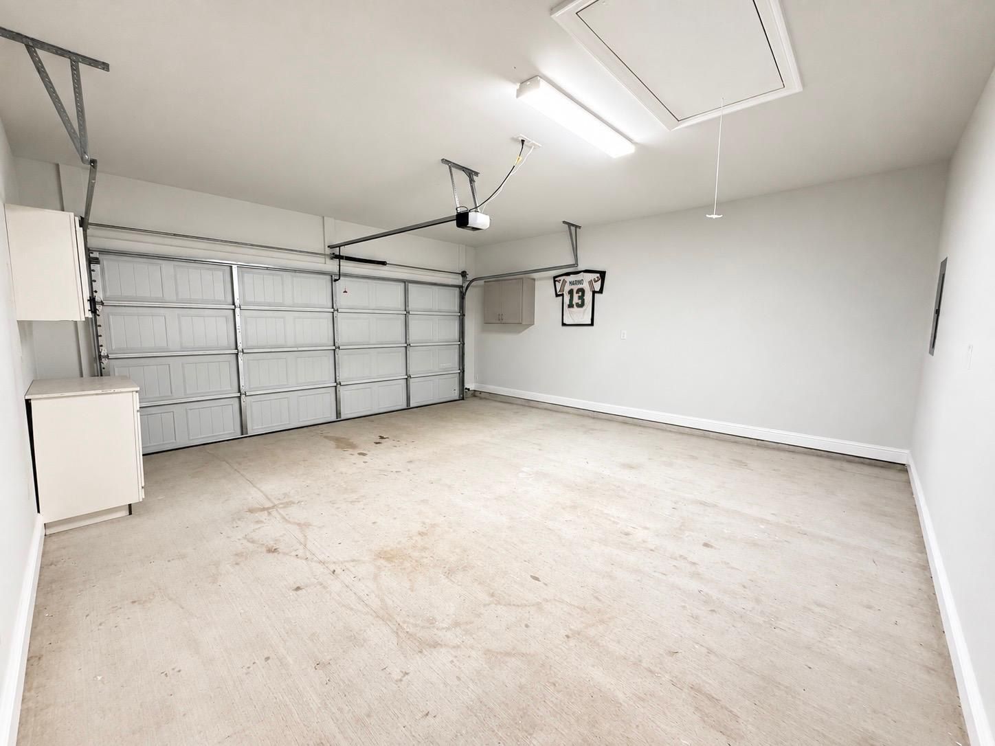 Een garage met een witte deur, een projector bevestigd aan het plafond en een lamp aan de muur.