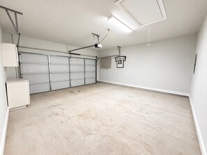 A garage with a white door, a ceiling-mounted projector, and a wall-mounted light fixture. - Tigers Geaux Crazy at The Wild LSU Jungle - KC7049 (Baton Rouge)