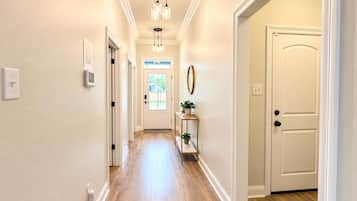 A hallway with a door at the end, a light fixture above, and a small table with a plant.