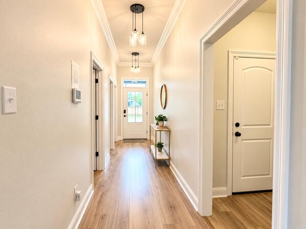 Un couloir avec une porte au fond, un luminaire au plafond et une petite table sur laquelle est posée une plante.
