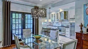 Une cuisine moderne avec des meubles blancs, un îlot central et un coin repas comprenant une table et des chaises en verre.