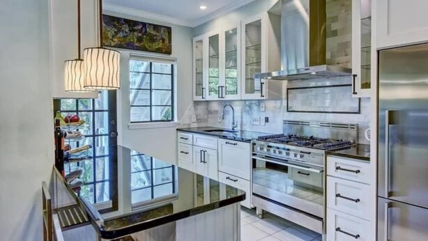 Une cuisine moderne avec des meubles blancs, une cuisinière en acier inoxydable et une grande fenêtre.