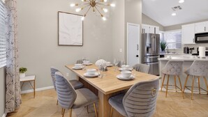 A modern kitchen with stainless steel appliances, a wooden dining table, and grey upholstered chairs. - Spectacular 5BR Home: Pool and Relaxing Space! (North Las Vegas)