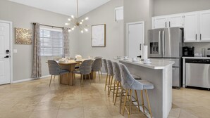 A modern kitchen with a central island, stainless steel appliances, and a dining area with a chandelier. - Spectacular 5BR Home: Pool and Relaxing Space! (North Las Vegas)
