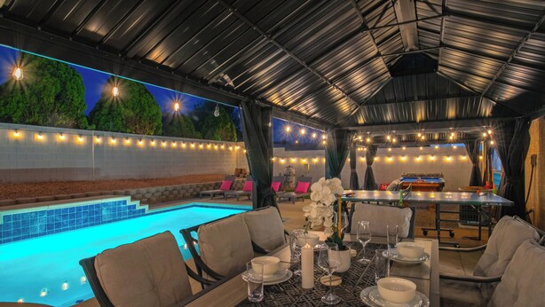 An outdoor dining area with a pool, tables set with plates and glasses, and string lights. - Spectacular 5BR Home: Pool and Relaxing Space! (North Las Vegas)
