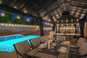 An outdoor dining area with a pool, tables set with plates and glasses, and string lights.