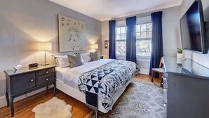 A bedroom with a bed, bedside tables, a TV, and a large window with curtains. - Historic Dilworth 3-Unit Stay | 6 King Beds + Parking | Near Atrium & Novant (Charlotte)