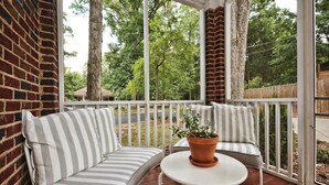 A covered patio with a brick wall, a white railing, and a seating area with striped cushions. - Historic Dilworth 3-Unit Stay | 6 King Beds + Parking | Near Atrium & Novant (Charlotte)