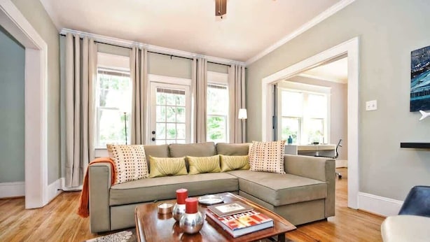 A modern living room with a sectional sofa, a coffee table, and a view of the outdoors through large windows. - Historic Dilworth 3-Unit Stay | 6 King Beds + Parking | Near Atrium & Novant (Charlotte)
