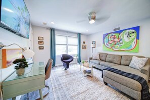 A modern living room with a glass desk, a grey sofa, and a colorful abstract painting.