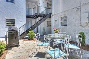 A patio area with a round glass table and metal chairs, a barbecue grill, and a staircase leading to an upper floor.