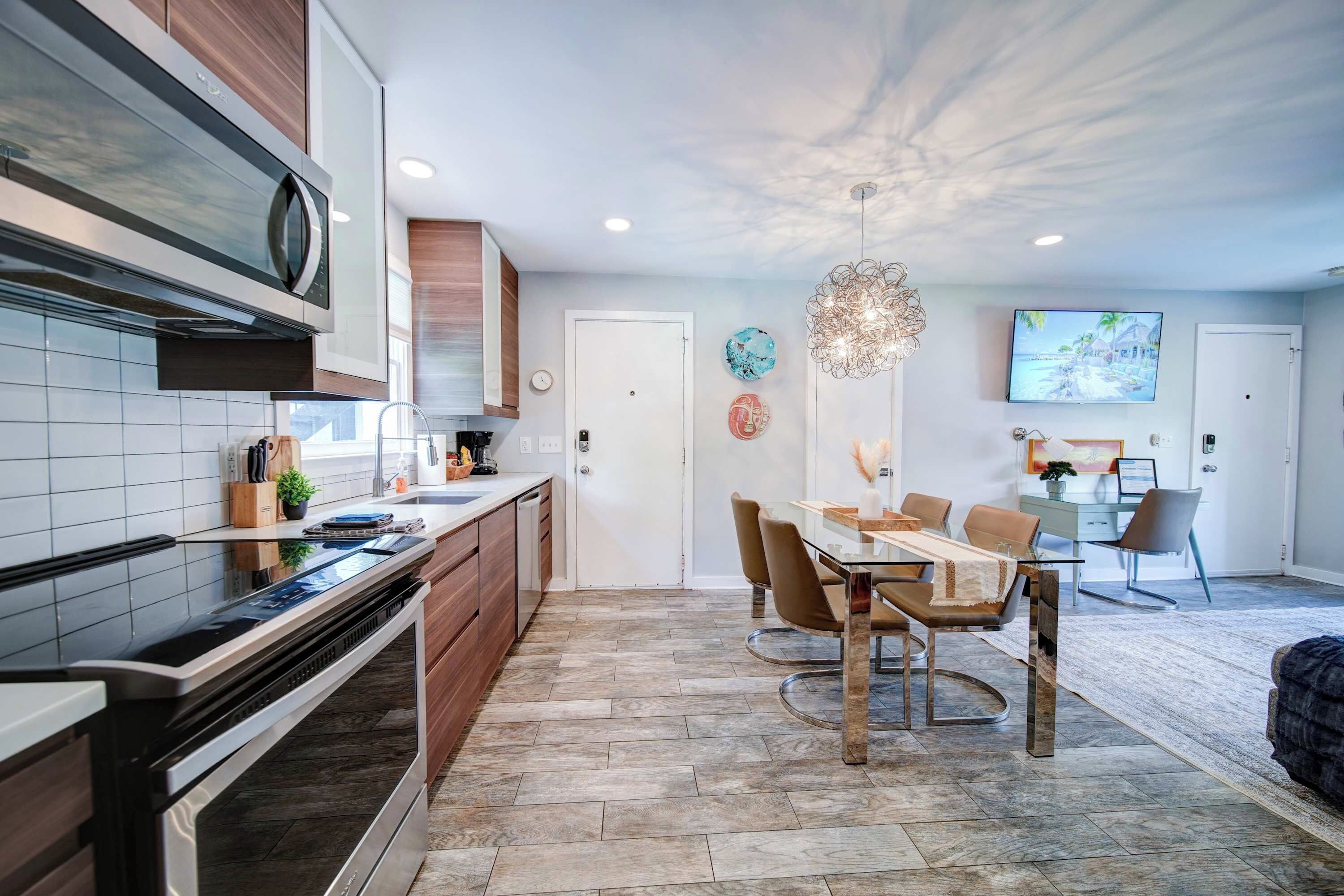Een moderne keuken met een ingebouwde oven, een eethoek met een glazen tafel en een aan de muur bevestigde televisie.