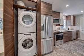 A modern kitchen with a built-in washer and dryer, stainless steel appliances, and wooden cabinetry. - Modern Myers Park 1BR · Ground Floor · Free Parking · near Atrium CMC & Uptown (Charlotte)
