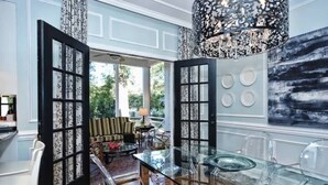 A modern kitchen with a glass dining table, black-framed doors, and a decorative chandelier.
