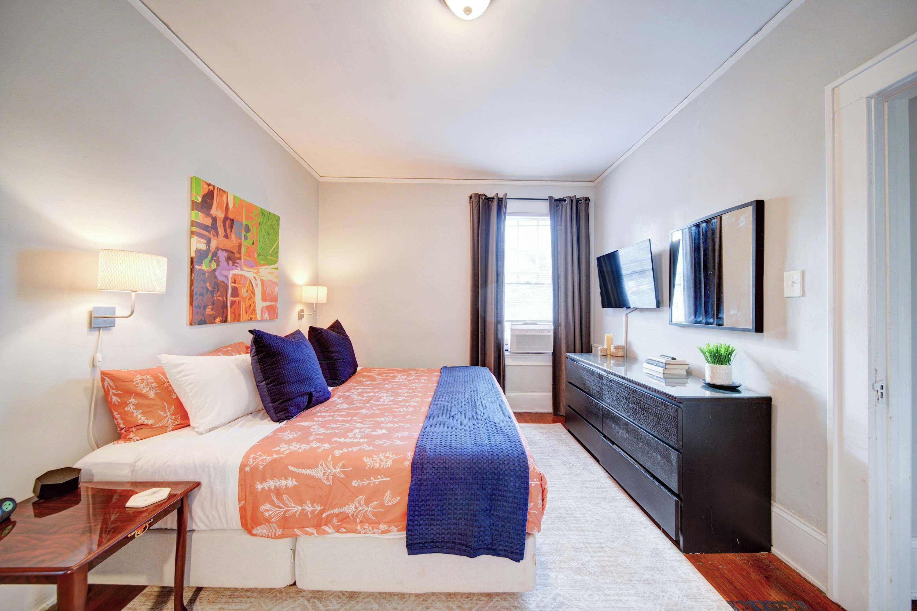 A bedroom with a bed, bedside tables, a dresser, a TV, and artwork on the wall.