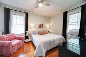 A bedroom with a bed, a sofa, a TV, and a ceiling fan.