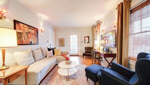 Una sala de estar con sofá, sillón, mesa de centro y obras de arte en las paredes.