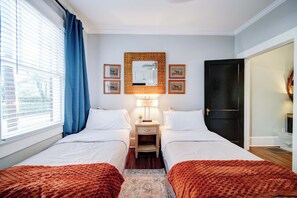 Habitación de hotel con dos camas, una mesita de noche con lámpara, un espejo y cuadros en la pared.