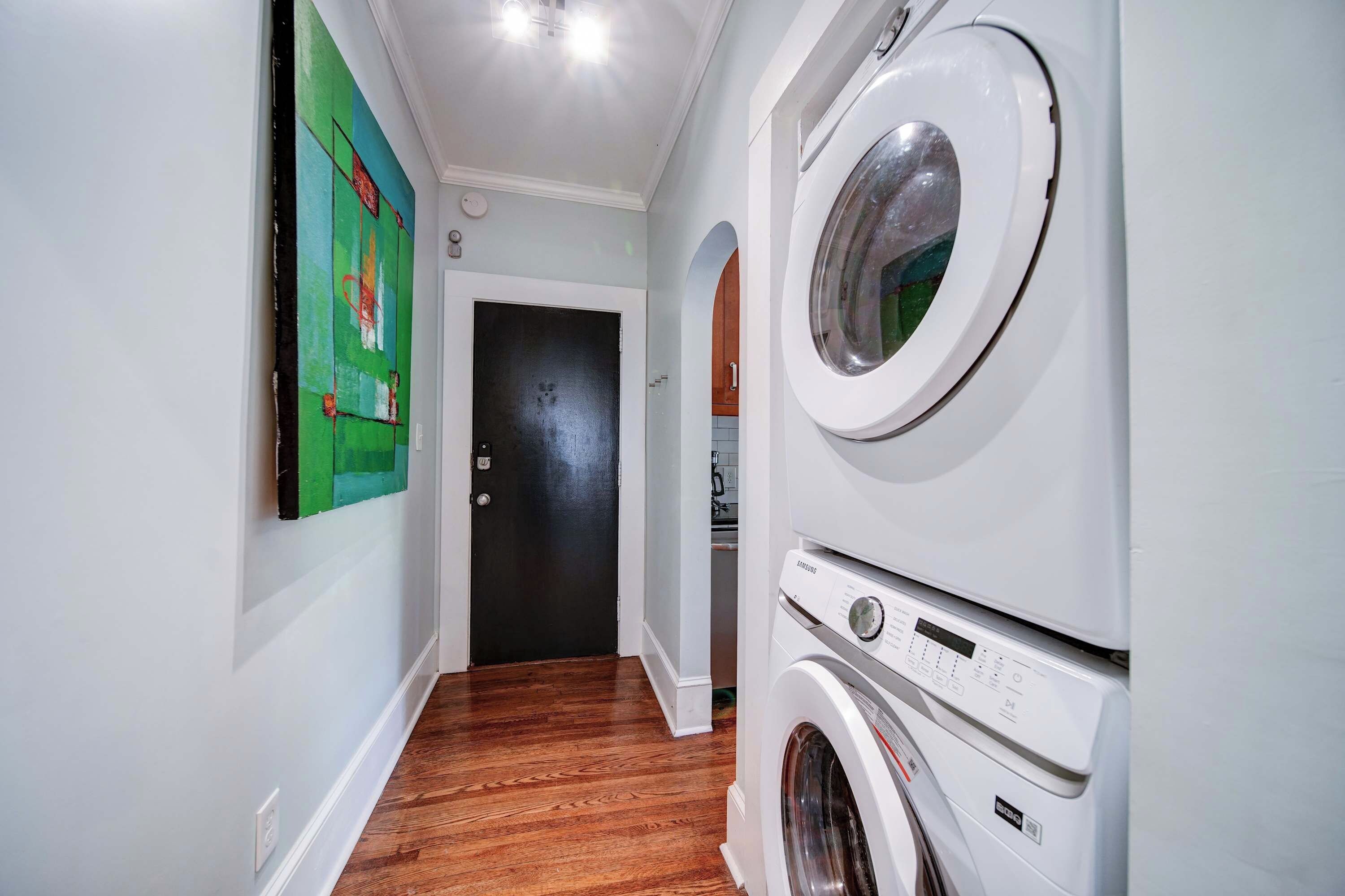 A laundry room with stacked washers and dryers, a door leading to another room, and a painting on the wall.