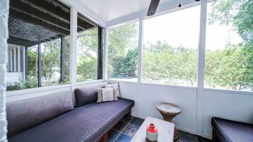 A sunroom with a cushioned seating area, a small table, and a view of greenery outside.
