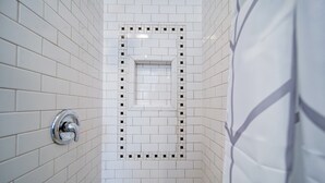 A bathroom with white tiled walls and a shower area. - The Home Collection: Historic Myers Park 2BR/2BA | Step-Free | Screened Porch (Charlotte)