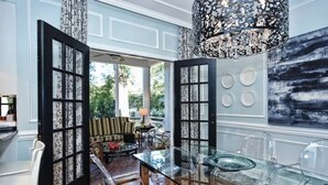 Ein modernes Interieur mit einem Glastisch, schwarzen Türrahmen und einem großen, abstrakten Gemälde.