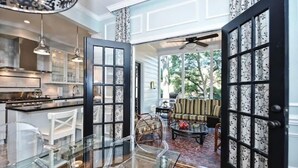 Eine geräumige Küche mit modernen Geräten, ein Essbereich mit Glastisch und ein Wohnzimmer mit Sofa und gemusterten Vorhängen.