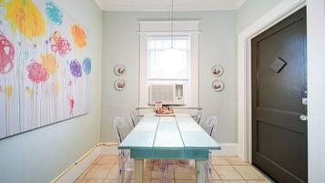 A dining area with a light blue table and chairs, a large abstract painting on the wall, and a dark door to the right.