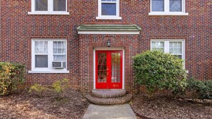 Un edificio de ladrillo de dos pisos con una puerta roja y un porche pequeño.
