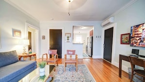 A living room with a sofa, chairs, a coffee table, and a rug. There is a kitchen in the background with cabinets and appliances. - Historic Dilworth 1BR Apartment: King Suite Near Atrium Health & Uptown (Charlotte)