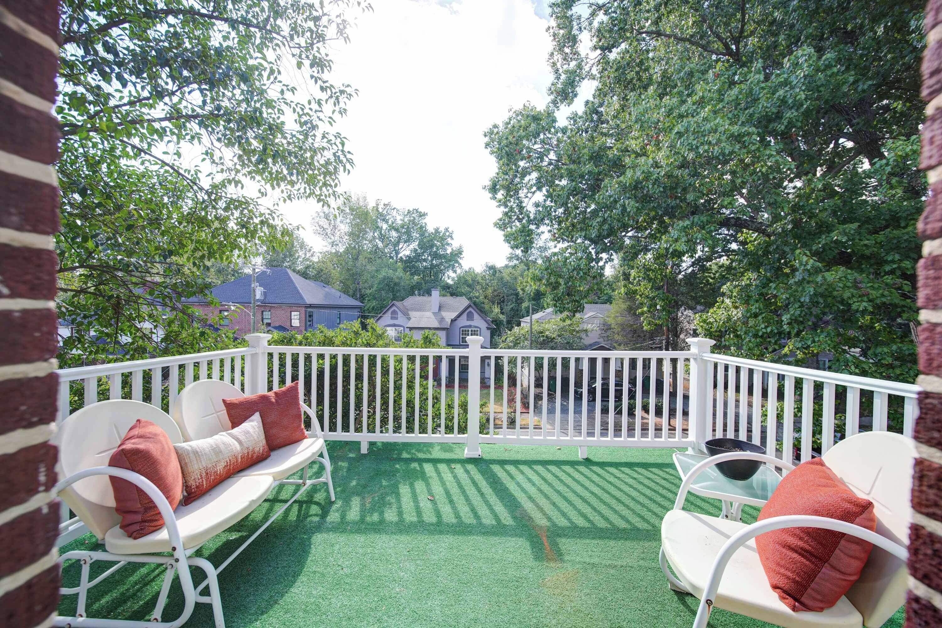 A balcony with a white railing, two white chairs with red cushions, and a green artificial turf floor.