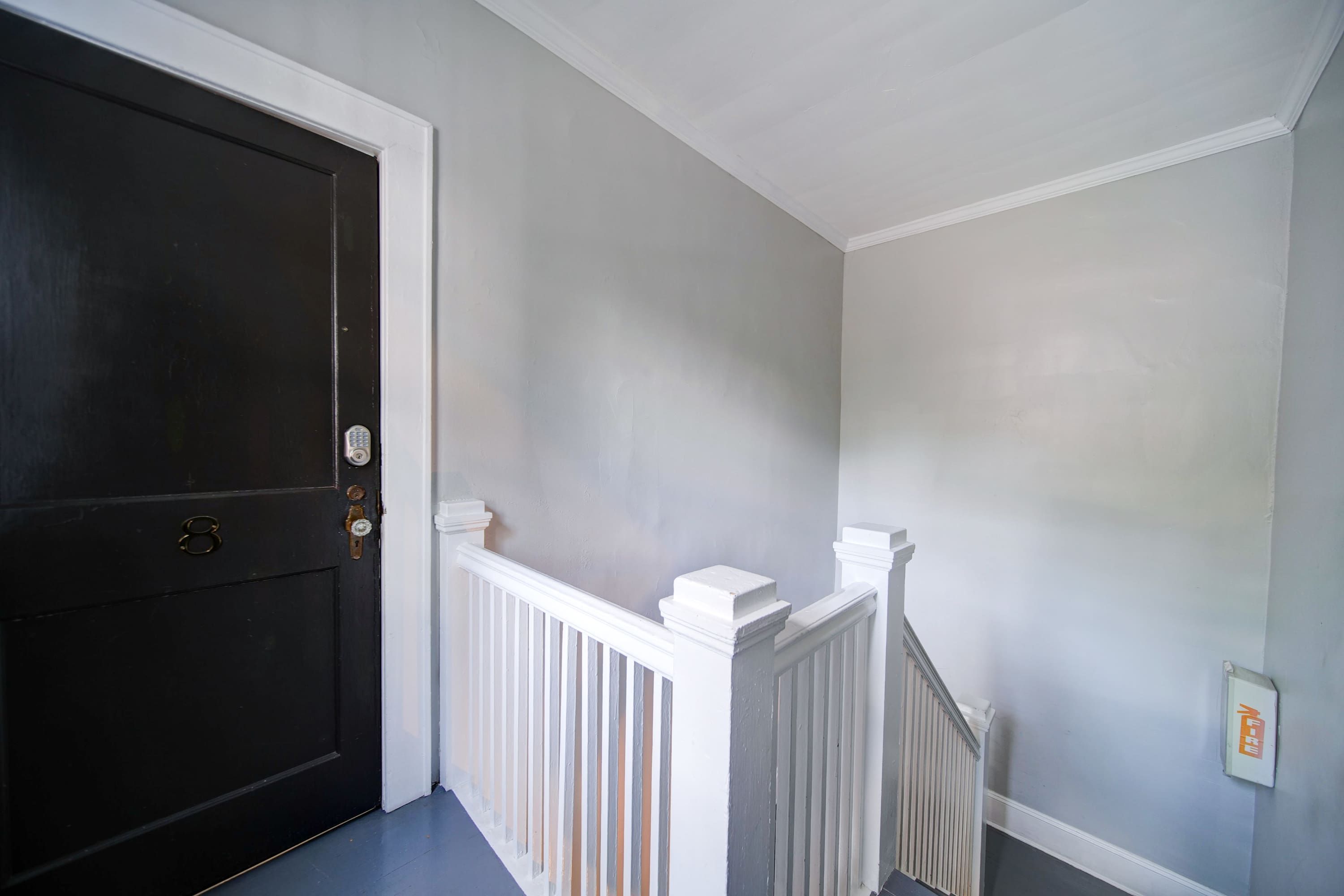 A hallway with a dark door, white railings, and a light-colored wall.