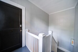 Een gang met een donkere deur, witte leuning en een lichtgekleurde muur.