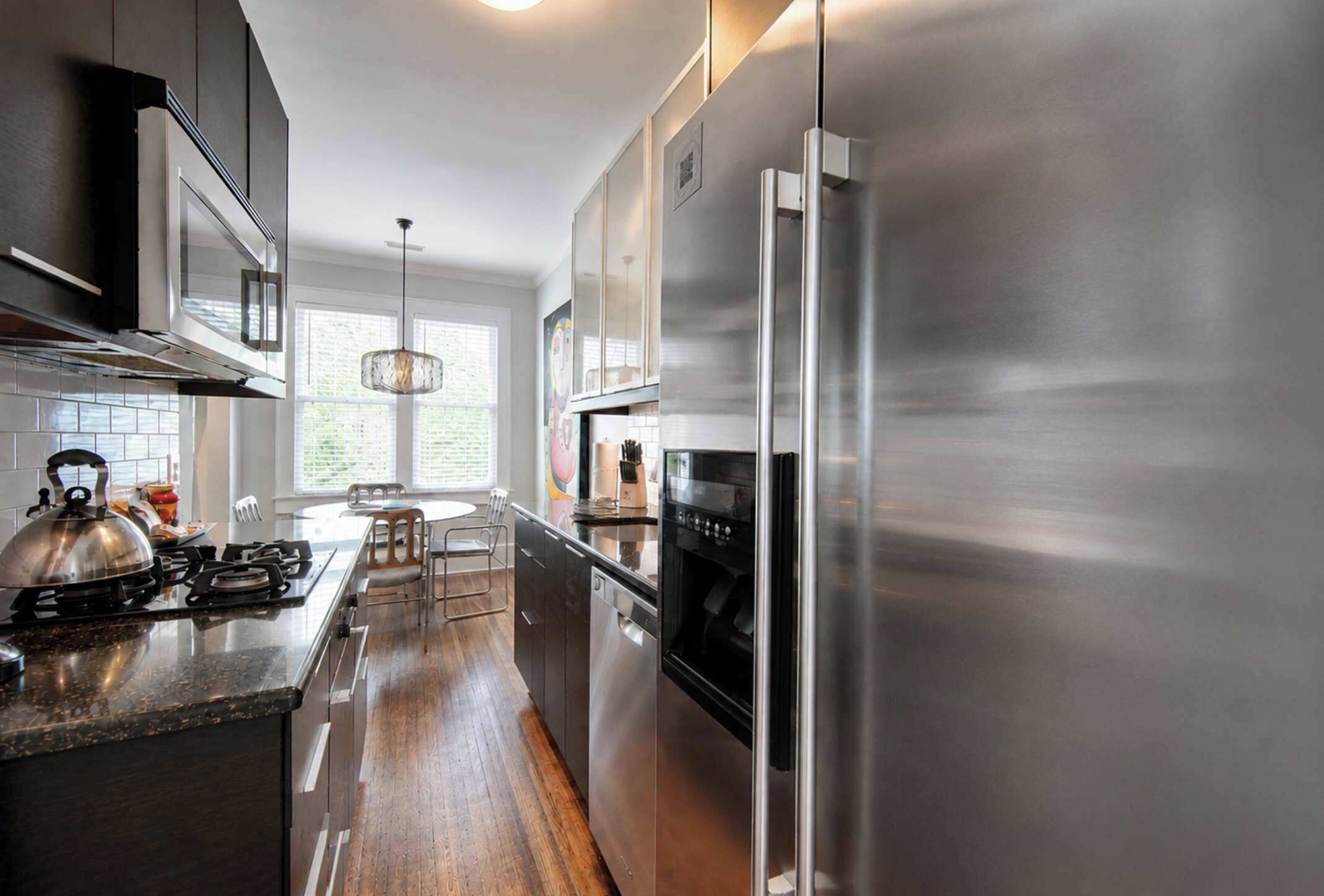 A modern kitchen with stainless steel appliances, a wooden floor, and a large window providing natural light.