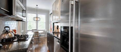 A modern kitchen with stainless steel appliances, a wooden floor, and a large window providing natural light.